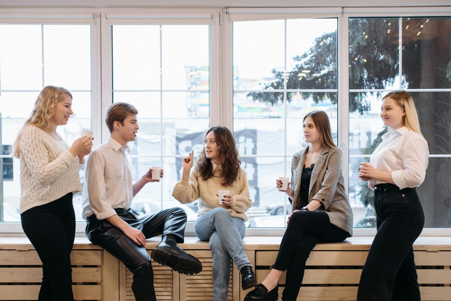 Kollegen im Gespräch: Fünf junge Menschen unterhalten sich entspannt bei einer Kaffeepause im Büro – Symbolbild für gelungene Kommunikation, Teamdynamik und konstruktives Miteinander nach einer Mediation.